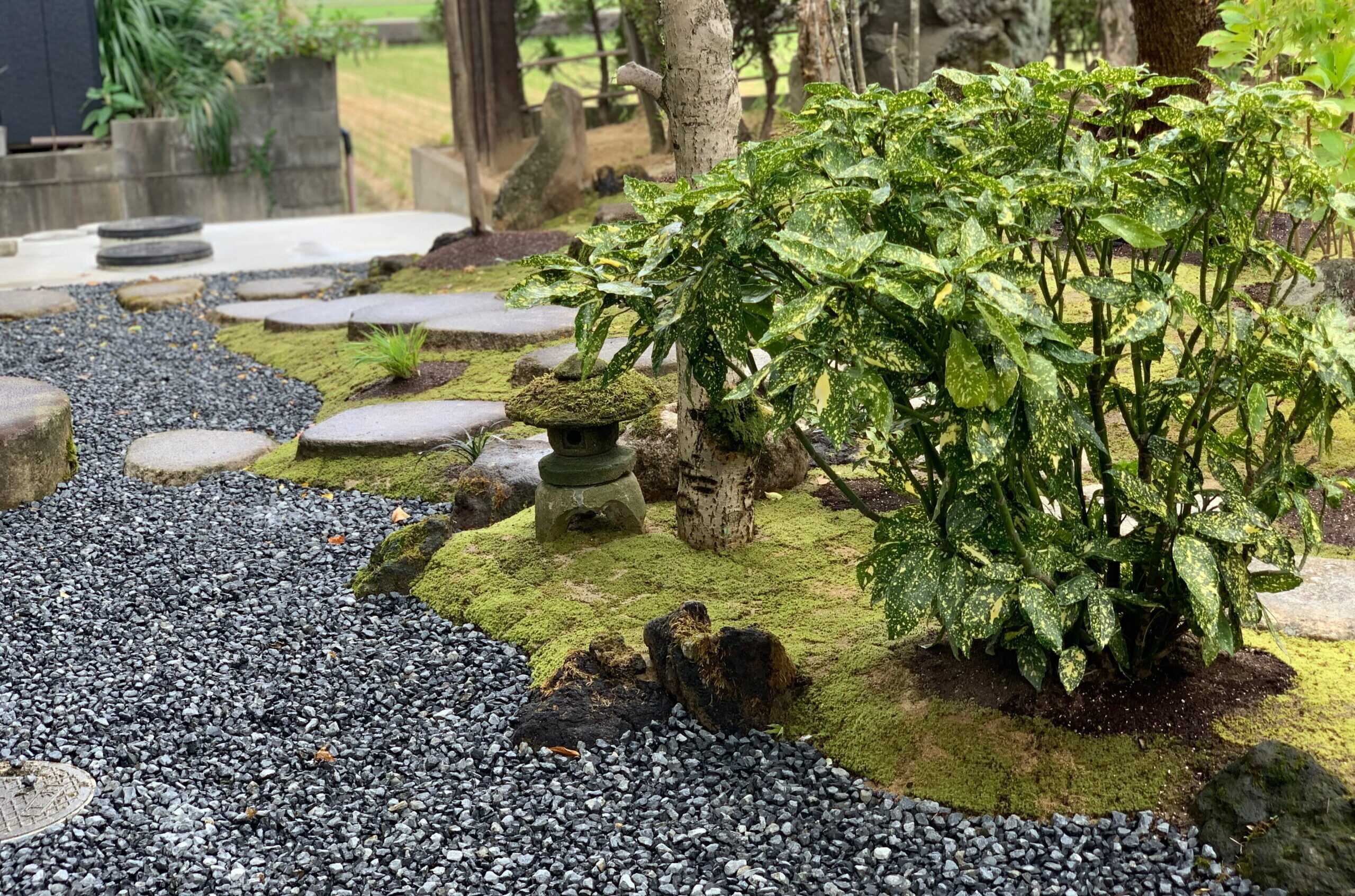 施工後の庭。苔むした地面に置かれた石灯籠と、飛び石、玉砂利の小径