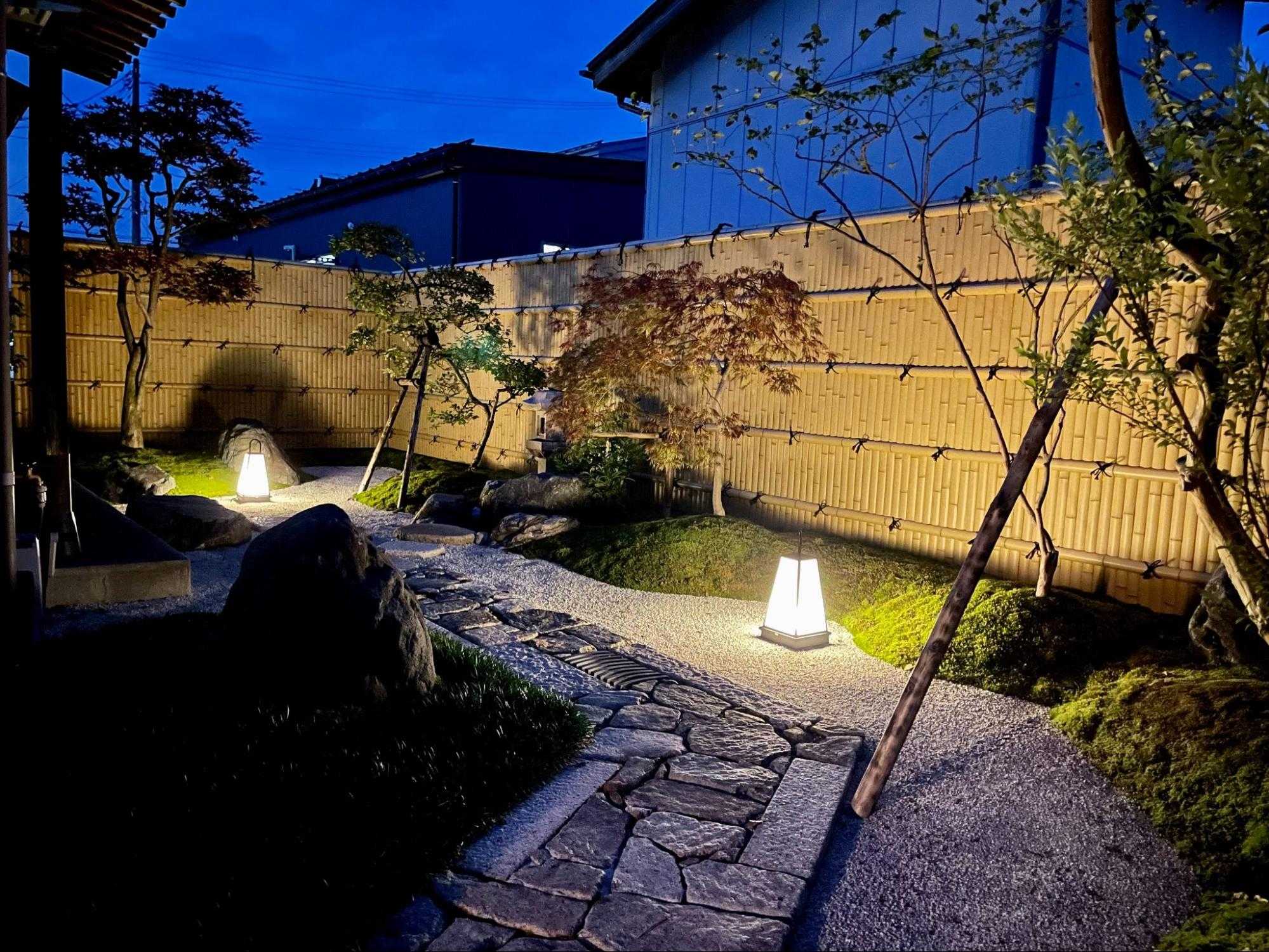 夜にライトアップされた施工後の和風庭園。行灯型の照明に照らされた石畳と苔や竹垣